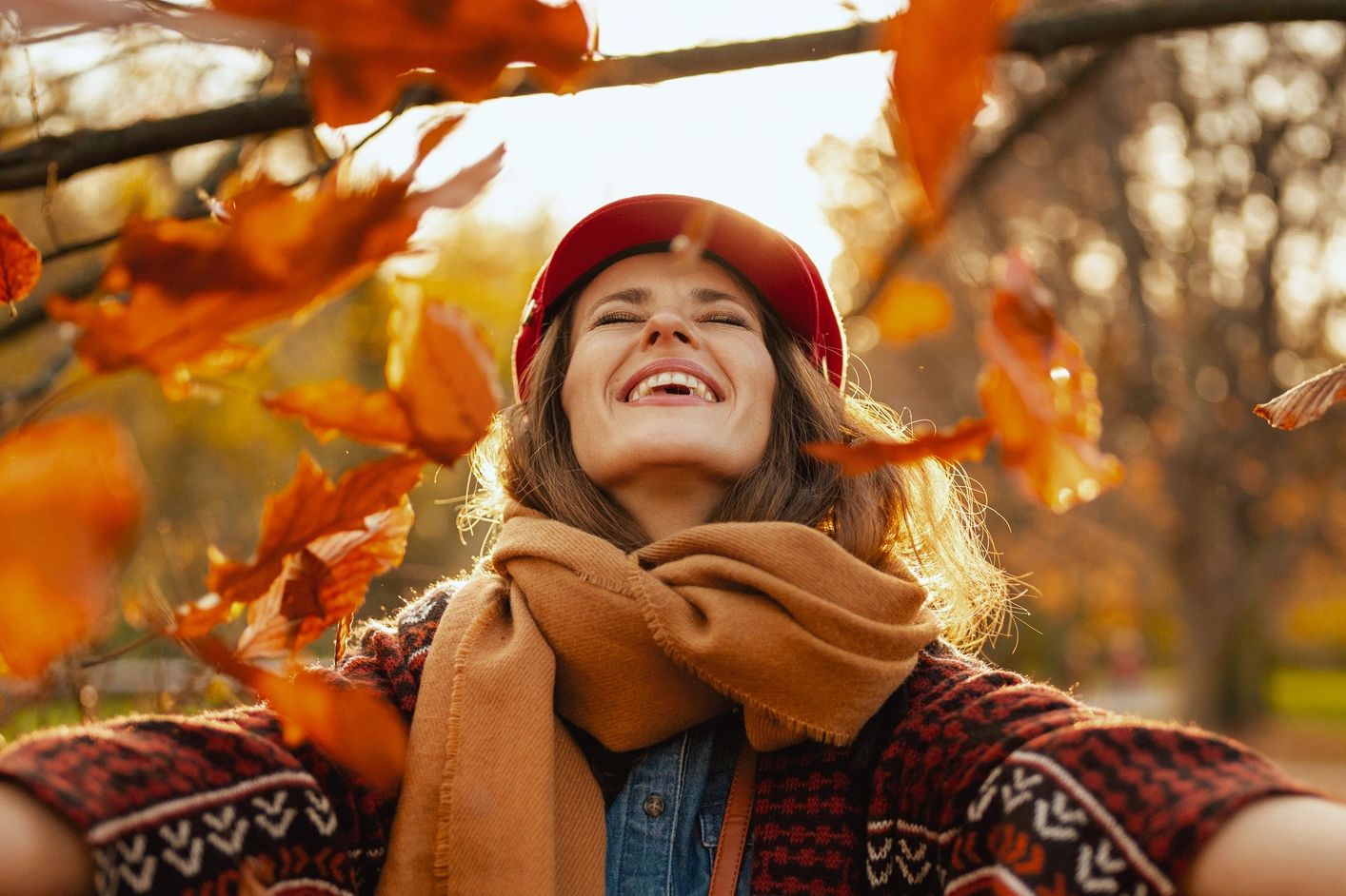 Woman enjoying autumn outdoors with falling leaves.