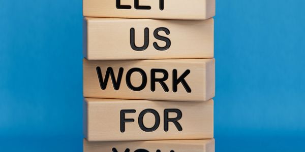 Stacked wooden blocks spell out 'LET US WORK FOR YOU' against a blue background.