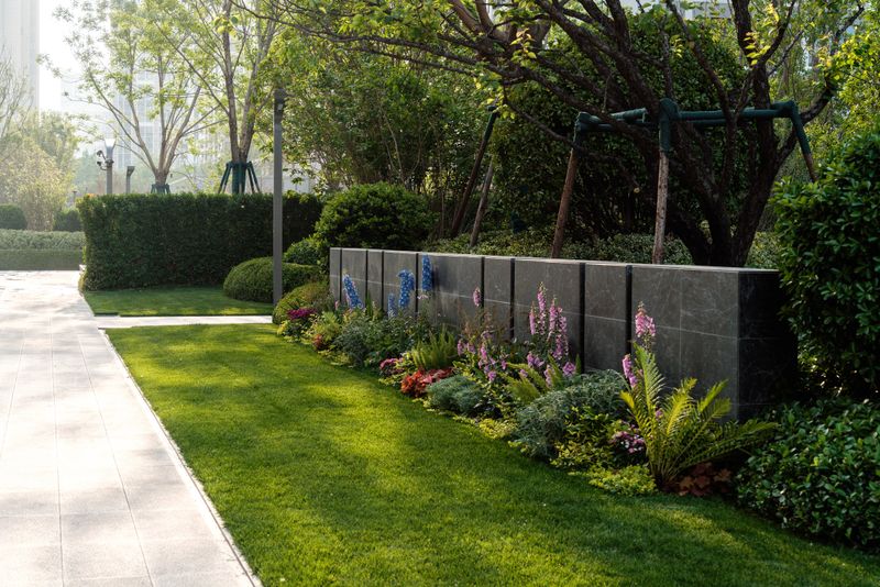 Colorful flower border and granite feature wall next to a sunlit grass path in a landscaped residential garden.