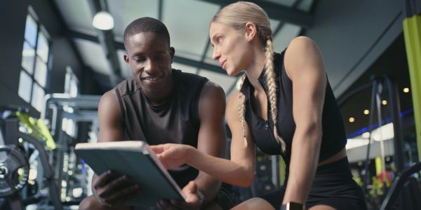 Two fit individuals discussing workout plans on a tablet at the gym.