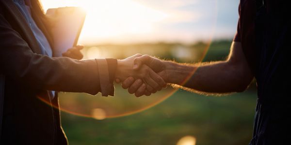 Two people shaking hands outdoors during sunset, symbolizing agreement.