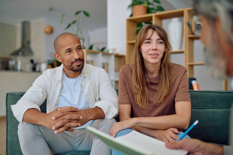 Young couple engaging with a senior financial advisor, taking notes during a home visit while discussing investment and retirement planning