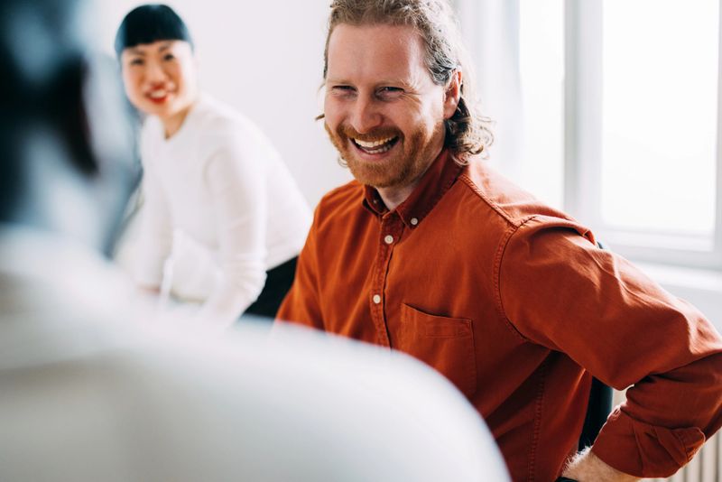 Colleagues enjoying positive interactions during a workplace meeting in a cheerful, collaborative setting. The image portrays teamwork, communication, and office camaraderie with a focus on professional relationships and workplace happiness.