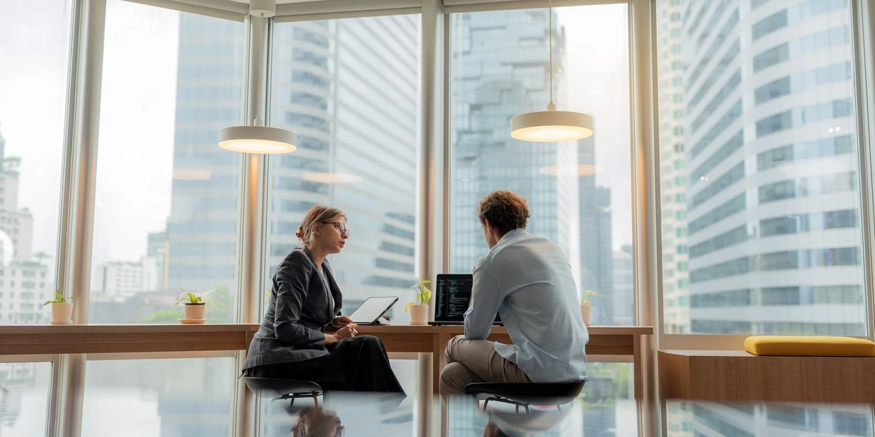 Two professionals discussing work in a modern office with city views.