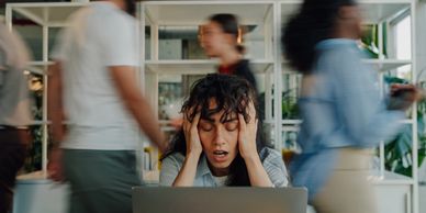 Stressed woman overwhelmed by busy office environment with blurred people moving around.