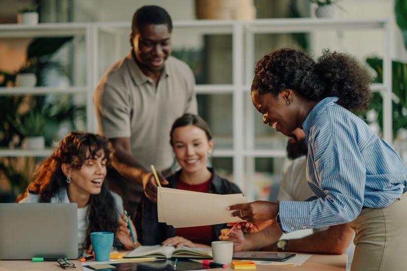 Group of happy colleagues reviewing paperwork together in a modern office, demonstrating teamwork and collaboration