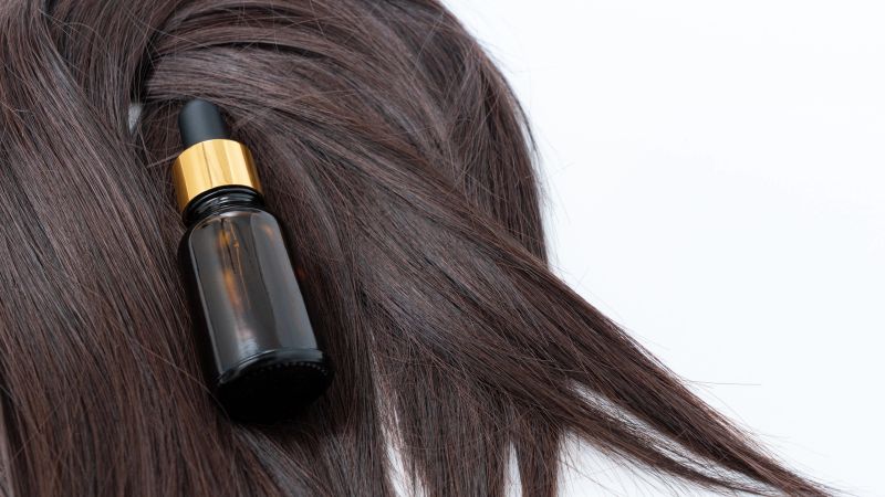 Dark, lustrous hair features a dropper bottle of nourishing oil placed on the strands, highlighting the importance of healthy hair care routines