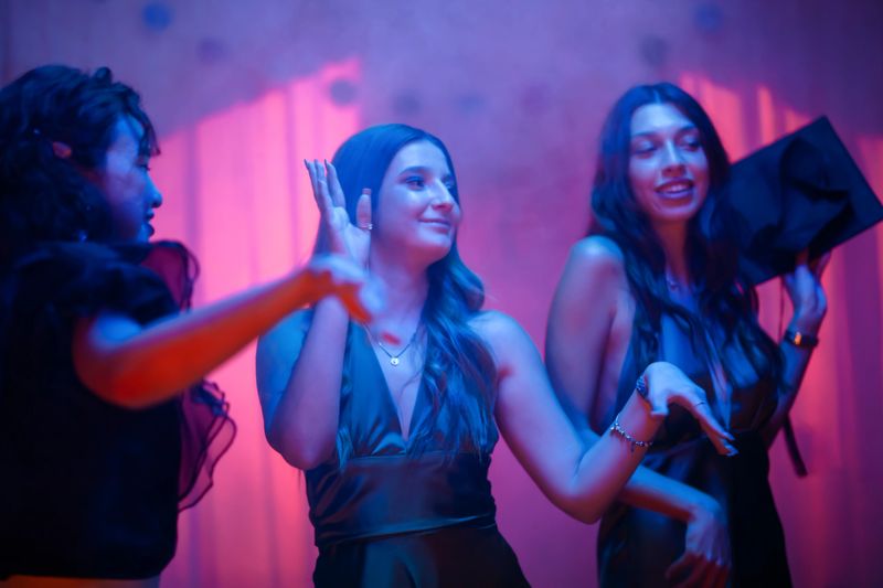 Three stylish women enjoying a vibrant party under colorful neon lighting, exuding joy.