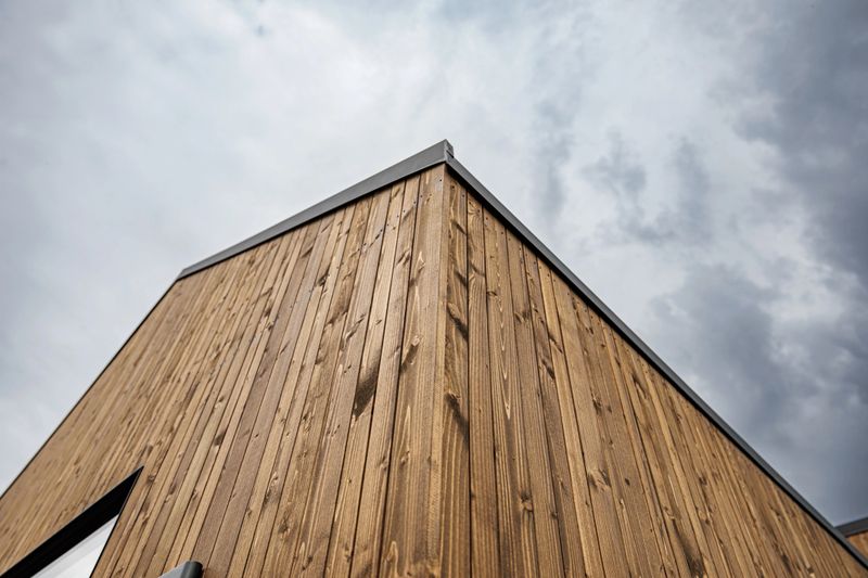 Close-up view of a modern tiny house corner with vertical timber cladding, black trim, and minimalist design, showcasing eco-friendly sustainable architecture