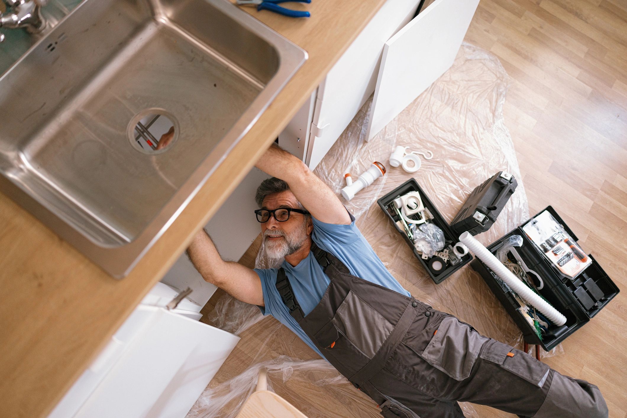 A plumber repairing kitchen sink pipes under the cabinet.