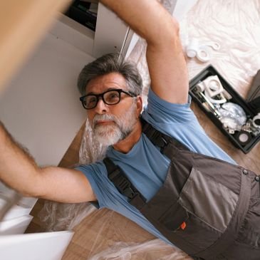 Man fixing a cabinet wearing overalls and glasses.