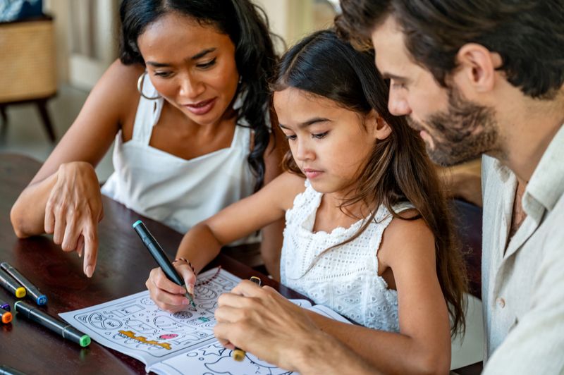 A family bonds over a creative activity, sharing joy and togetherness while coloring vibrant illustrations in an indoor setting, fostering creativity and connections within a warm and collaborative environment.