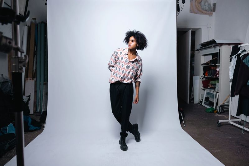 Portrait featuring a cheerful young man with curly, afro hair, crossing his arms and smiling brightly at the camera against a gray background