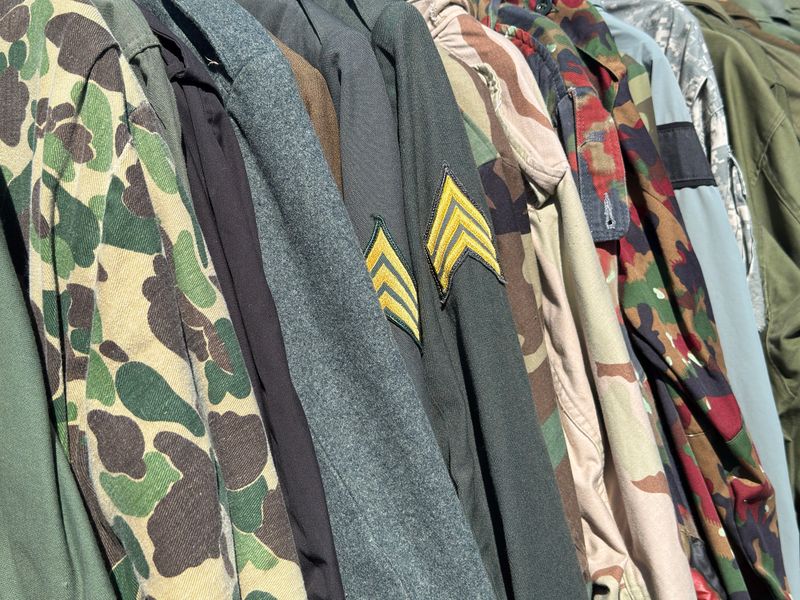 A close up of vintage military uniforms and jacket for sale at an outdoor vintage flea market
