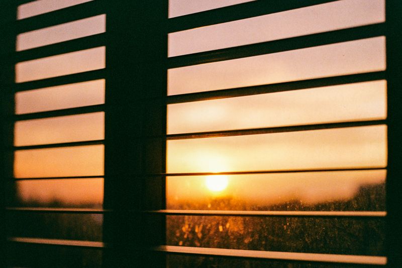 Film photograph of a glowing sunset seen through horizontal window blinds, creating a moody and nostalgic atmosphere. Kuala Lumpur.