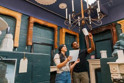 Man in black t-shirt and woman in white shirt observe papers while in a home.