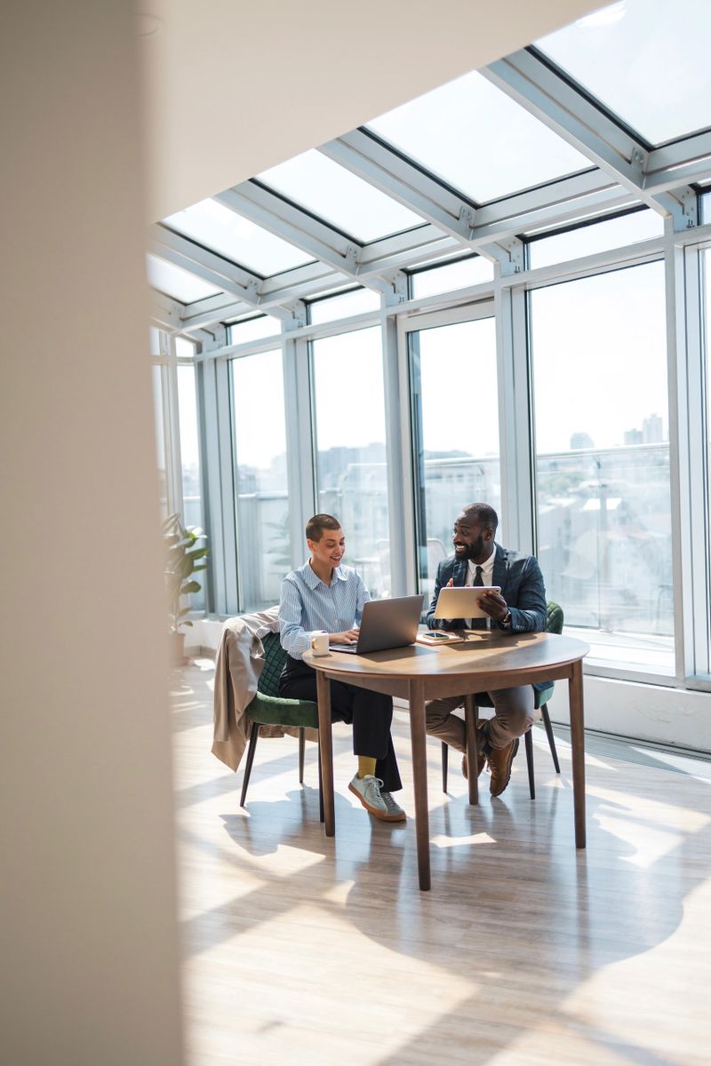 Business professionals collaborate at a table in a bright, modern office with large glass windows.
