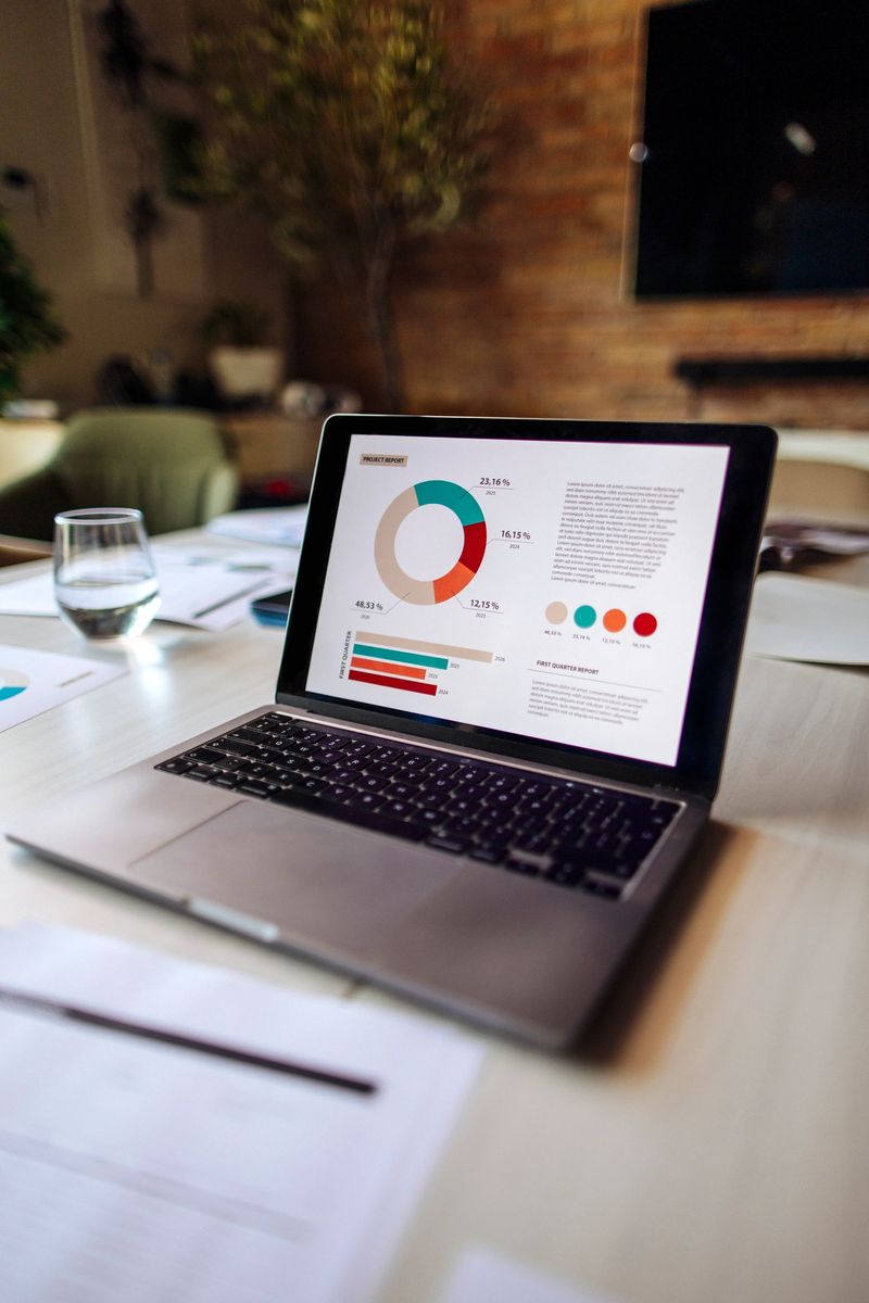 A stylish office desk featuring a laptop with visible business charts, reports, and data visualizations, reflecting professional analysis in a modern and harmonious workplace setting.