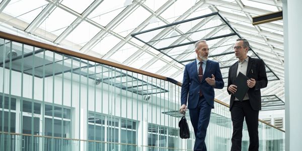 Two businessmen walking and talking in a modern office building.