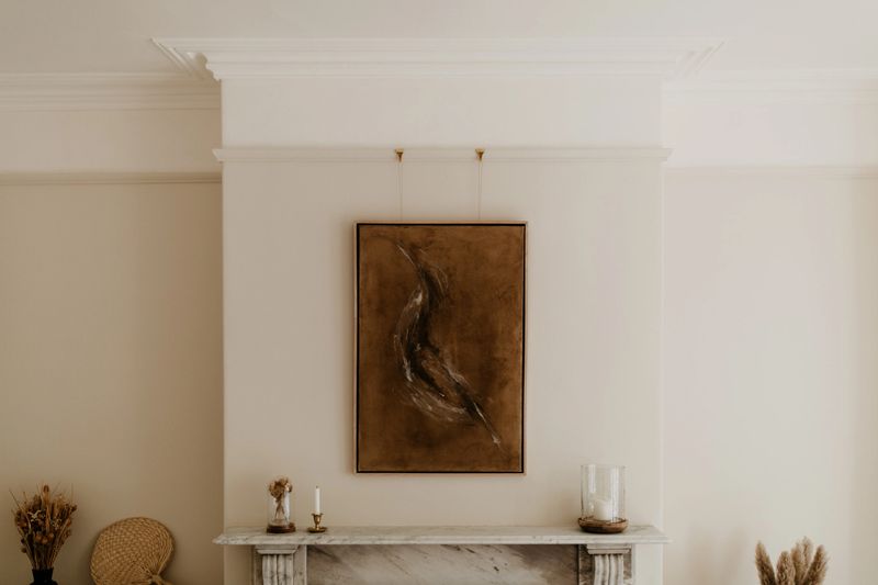 DIY abstract artwork hangs above a white marble fireplace in a minimalist interior setting. The scene features soft natural lighting, neutral tones, and clean architectural lines, blending contemporary design with timeless elegance—ideal for art-focused editorials, modern home decor marketing, or upscale lifestyle content.
