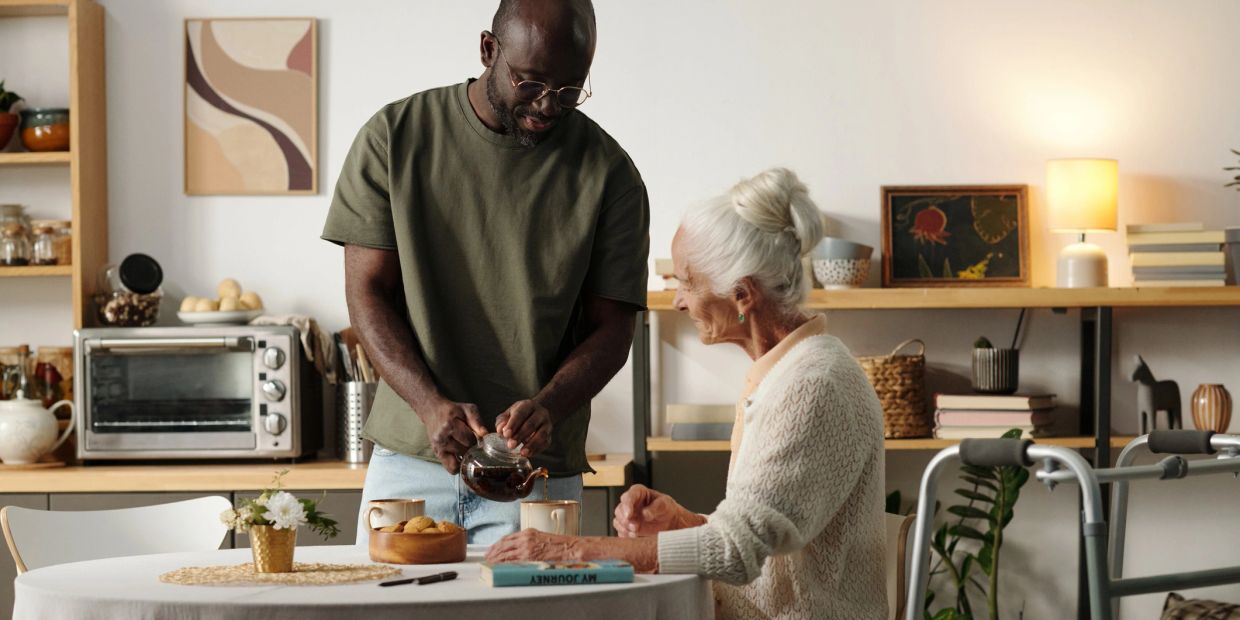 Man pouring tea for elderly woman at home.