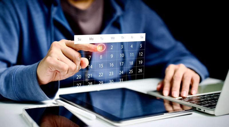 Business person scheduling with futuristic digital calendar interface on laptop and tablet, representing time management, planning, productivity, smart technology, and online organization tools.