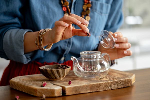 Person placing dried flower petals into a glass teapot.