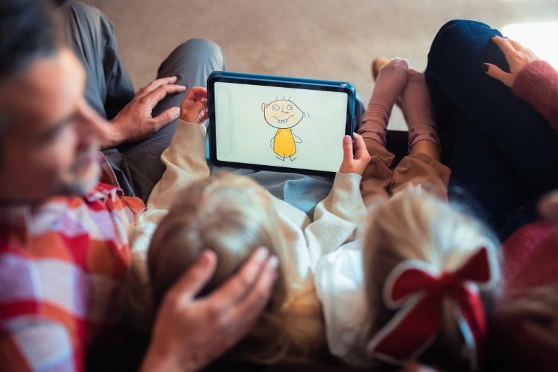 A family enjoys quality time together, viewing a colorful illustration on a tablet in their cozy living room. Featuring warm interactions and shared moments, this scene reflects connection and joyful bonding.