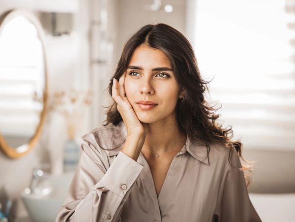 Young woman with thoughtful expression resting her face on her hand indoors.