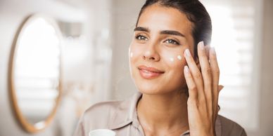 Woman applying moisturizer to calm and soothe skin.