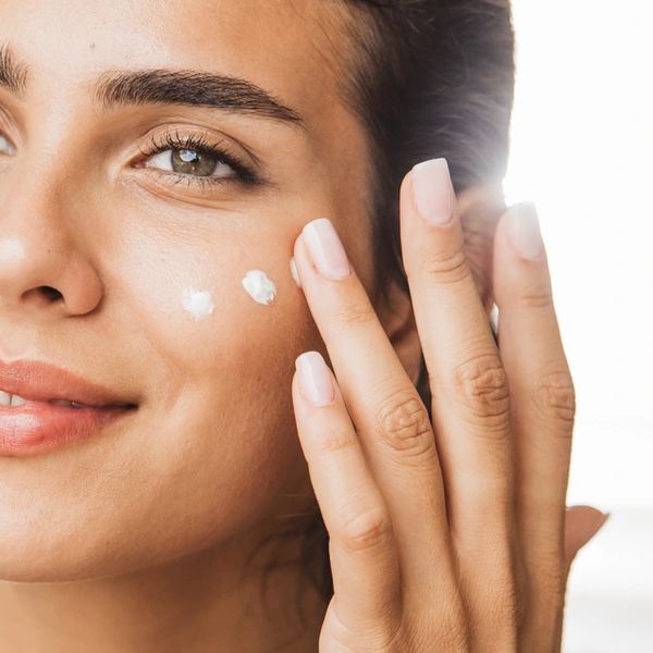 Woman applying moisturizer cream on her cheek with a gentle smile.