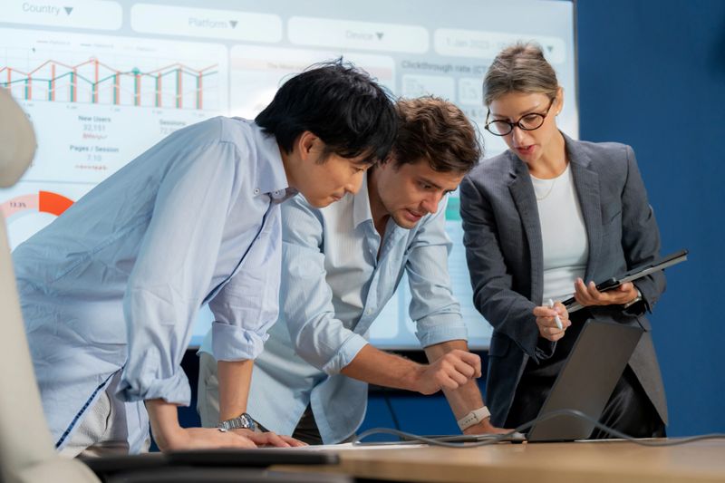 Multiracial office group working together in corporate meeting. Employees brainstorming, discussing strategy, marketing research, graphs, and innovation using technology for efficient planning and success.