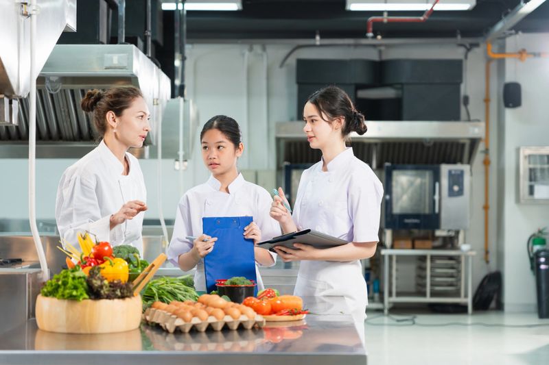 Female Culinary Students Practicing Cooking Skills with Fresh Ingredients in Training Kitchen, Professional Chef Teaching Women How to Prepare Dishes in Commercial Culinary Class
