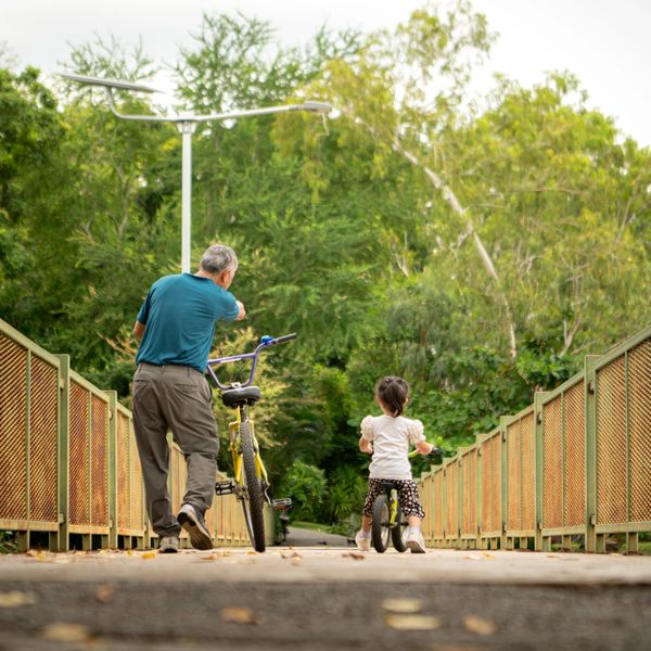 Elderly man and child biking on a bridge.