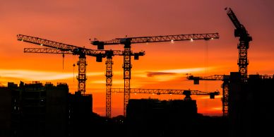 Construction cranes silhouetted against a sunset sky.