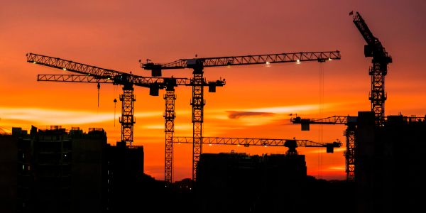 Construction cranes silhouetted against a sunset sky.
