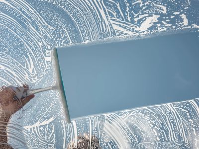 Hand cleaning a glass window with a blue squeegee.