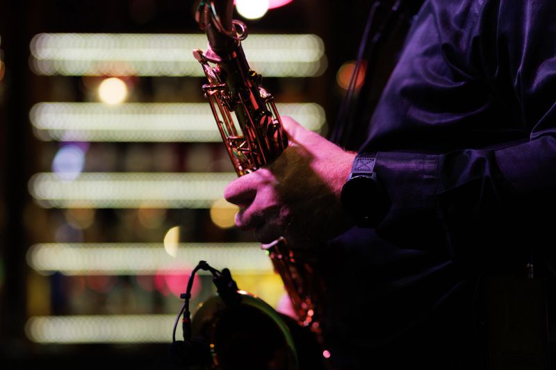 A skilled musician performing on stage, playing a saxophone in a vibrant jazz club setting with colorful ambient lighting creating an artistic and lively atmosphere.