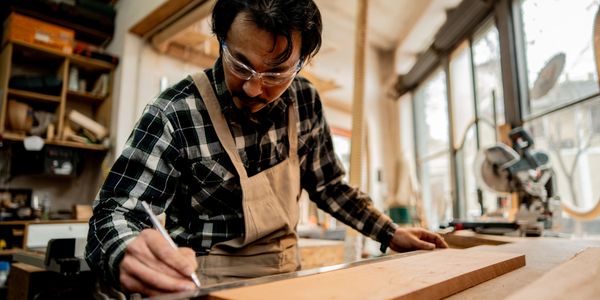 A man marking wood in a workshop with safety glasses and apron.