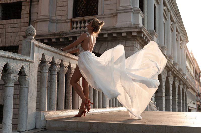Elegant woman in a flowing white dress on historic stone bridge in Venice, Italy.