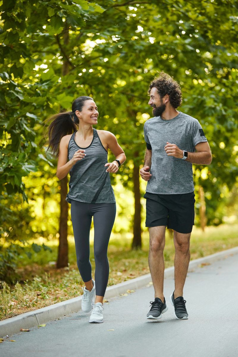 Young couple jogging together on a paved path in a green park, enjoying their healthy lifestyle