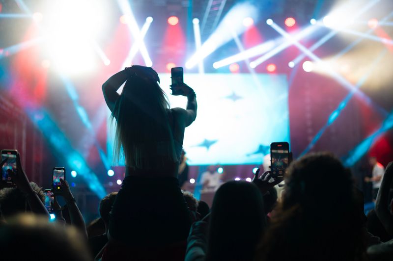 Young happy people in the audience dancing and cheering on the summer night concert.