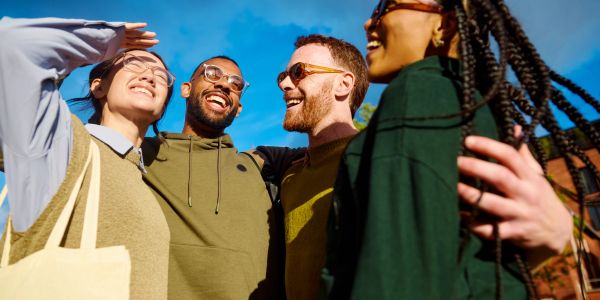 Four friends happily posing outdoors on a sunny day.