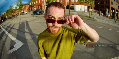 Man adjusting sunglasses on urban street.