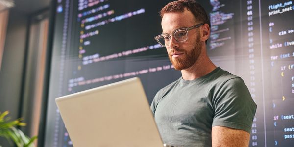 Man focused on coding with laptop and code on screen behind.
