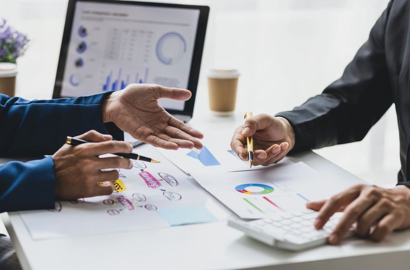 Business partner meeting with colleagues is discussing analysis of business financial situation and market share growth in order to plan budget and strategy to increase company profits.