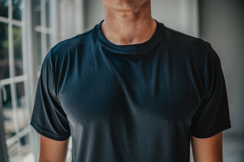 A young man models a sleek, black T-shirt in a well-lit, contemporary space. The garment highlights casual style, perfect for fashion-forward individuals seeking comfort and quality.