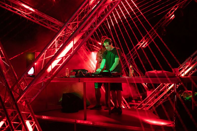 Two Dj's playing techno music on the futuristic stage at summer night concert.