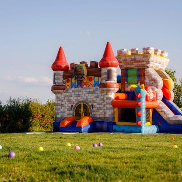 Colorful inflatable castle bounce house in a grassy yard with scattered balls.