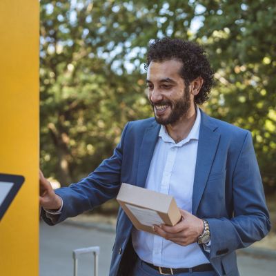 Man in suit using a parcel locker while holding a package.